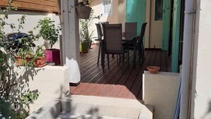 Une terrasse couverte avec une plateforme en bois, des sièges d’extérieur et des plantes en pot.