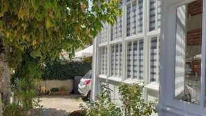 Une maison avec une allée pavée, une voiture blanche garée dans l’allée et un jardin où poussent différentes espèces de plantes.