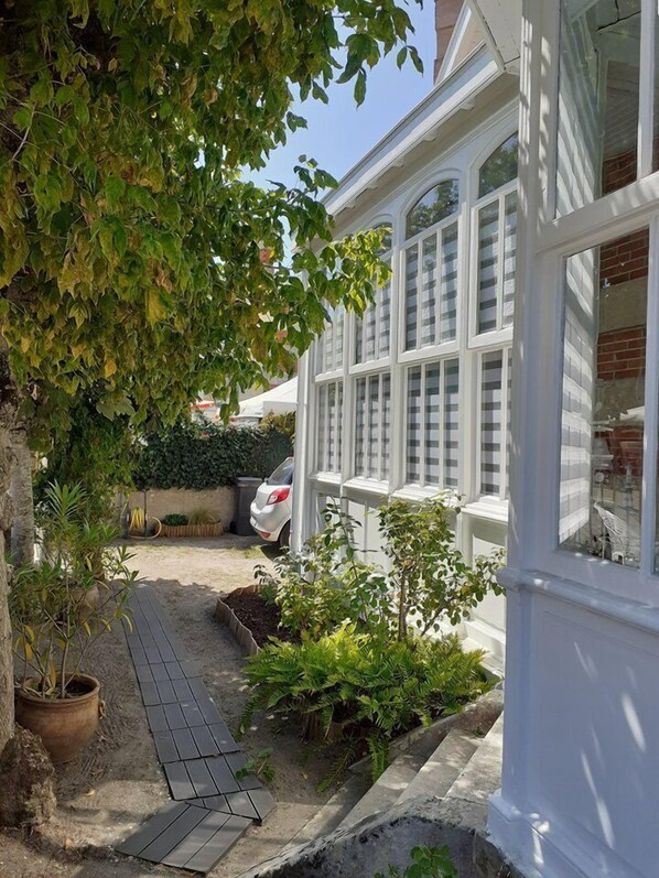 A house with a paved driveway, a white car parked in the driveway, and a garden with various plants.