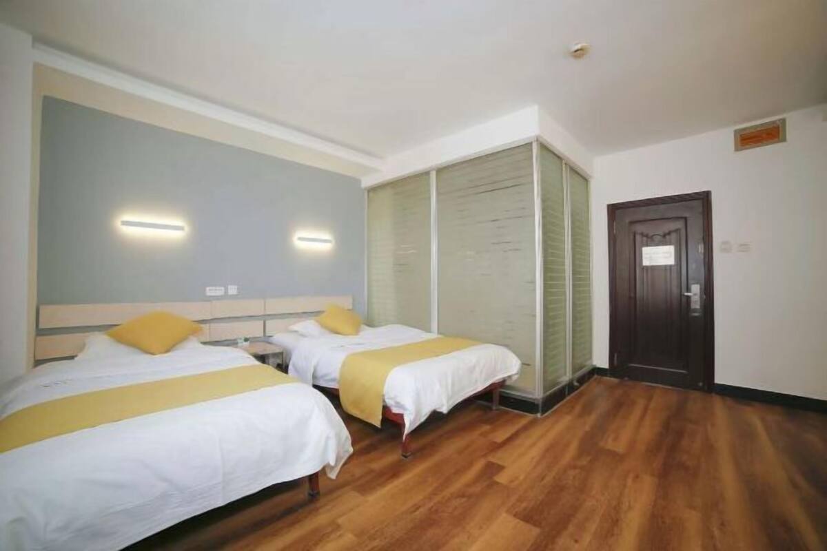 A hotel room with two beds, wooden flooring, and a sliding door.