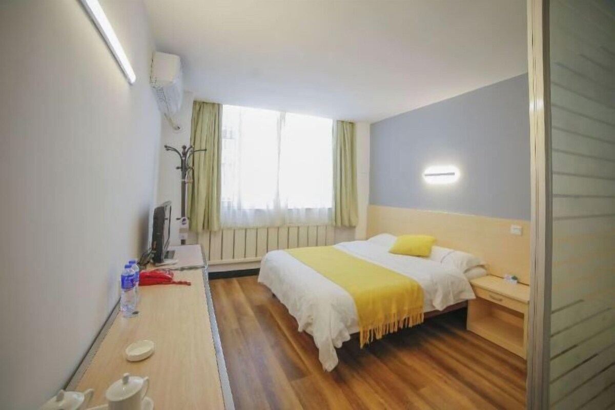 A hotel room with a bed, bedside table, and a window with curtains.