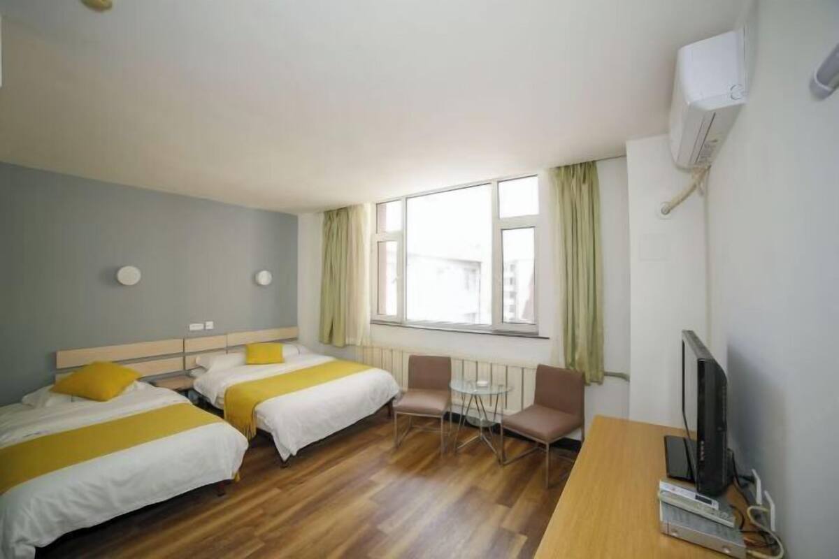 A hotel room with two beds, a small table, a chair, a TV, and a window with curtains.