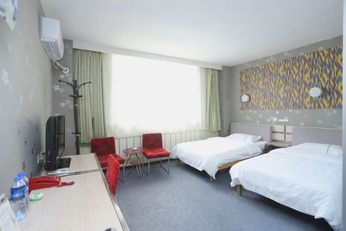 A hotel room with two beds, a desk with a computer, a TV, and a window with curtains.
