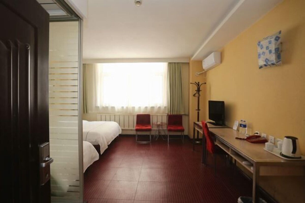 A hotel room with a bed, a desk, a chair, a television, and a window with curtains.