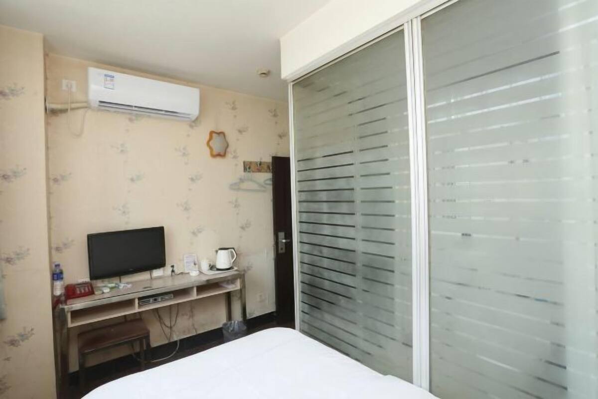 A hotel room with a bed, a TV, a desk with a computer, a coffee maker, and an air conditioner.