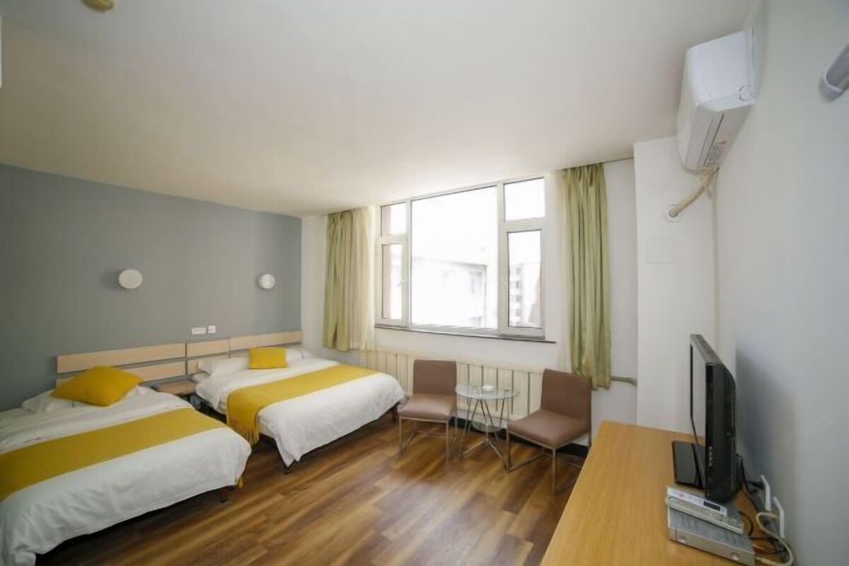 A hotel room with two beds, a small table, two chairs, a television, and a window with curtains.
