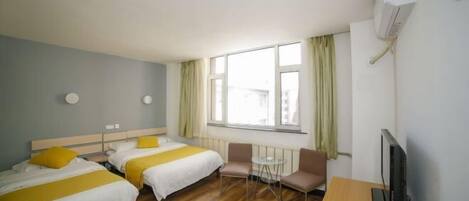A hotel room with two beds, a small table, two chairs, a television, and a window with curtains.