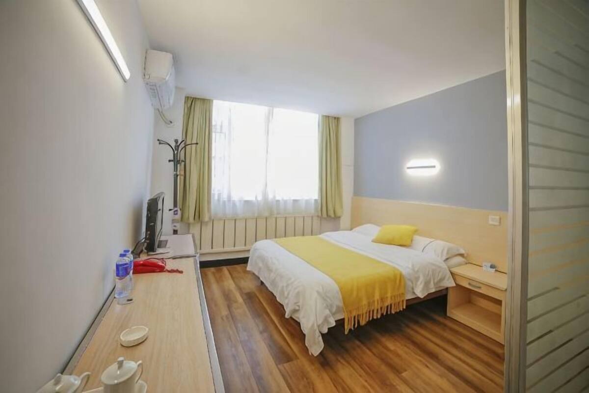 A hotel room with a bed, bedside table, lamp, and a window with curtains.