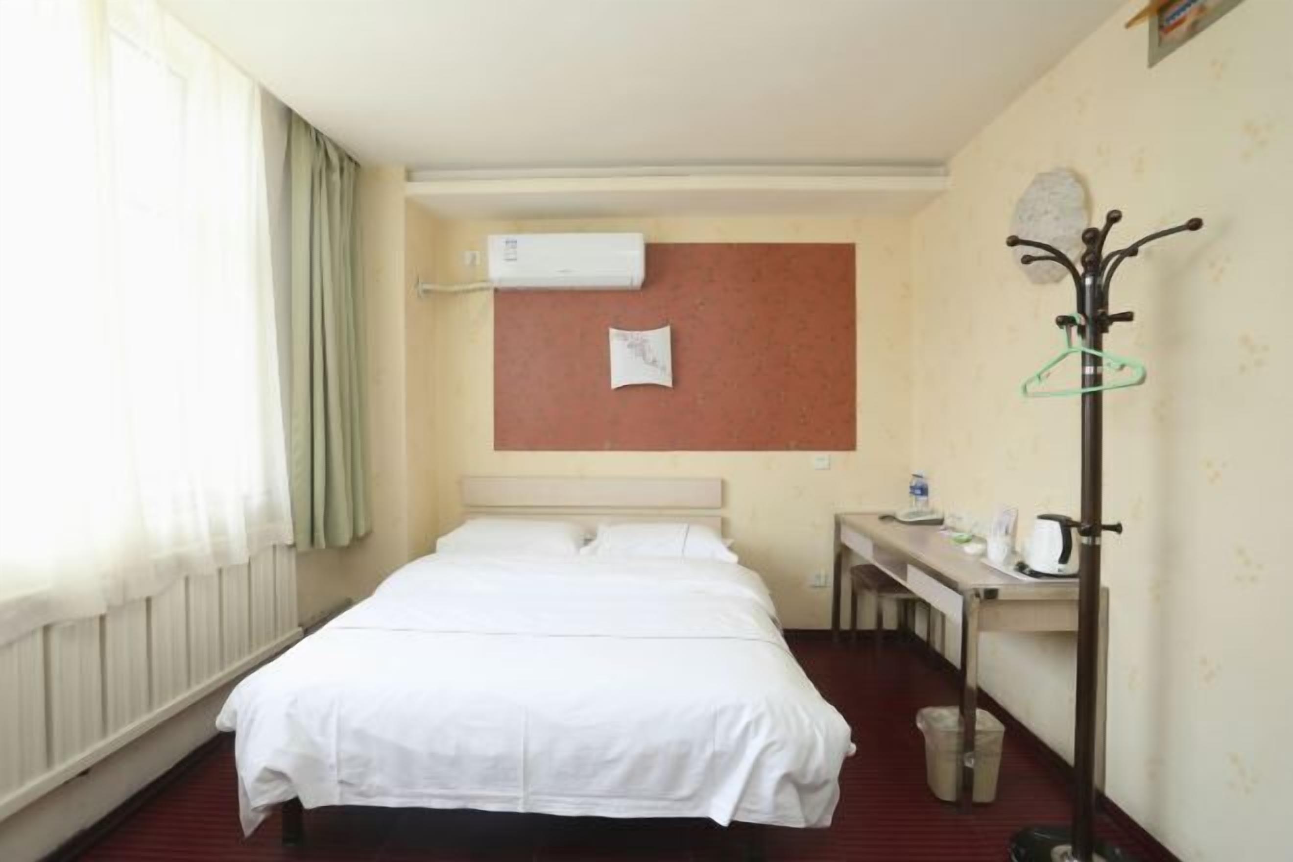 Une chambre d’hôtel avec un lit, un bureau doté d’une bouilloire et un porte-manteau.