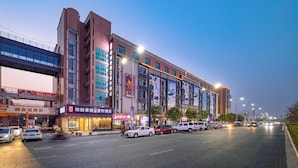A multi-story building with commercial establishments on the ground floor, a pedestrian overpass above, and vehicles on the street below. - Rezen Select Bellehaute (Suzhou)