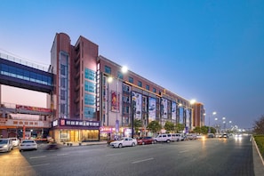 Un edificio de varios pisos con locales comerciales en la planta baja, un paso elevado encima y vehículos en la calle.