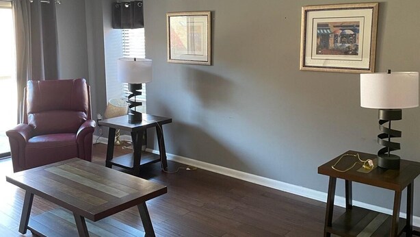 Una sala de estar con un sillón de cuero, una mesa de centro de madera, una mesita auxiliar con una lámpara y dos cuadros en la pared.