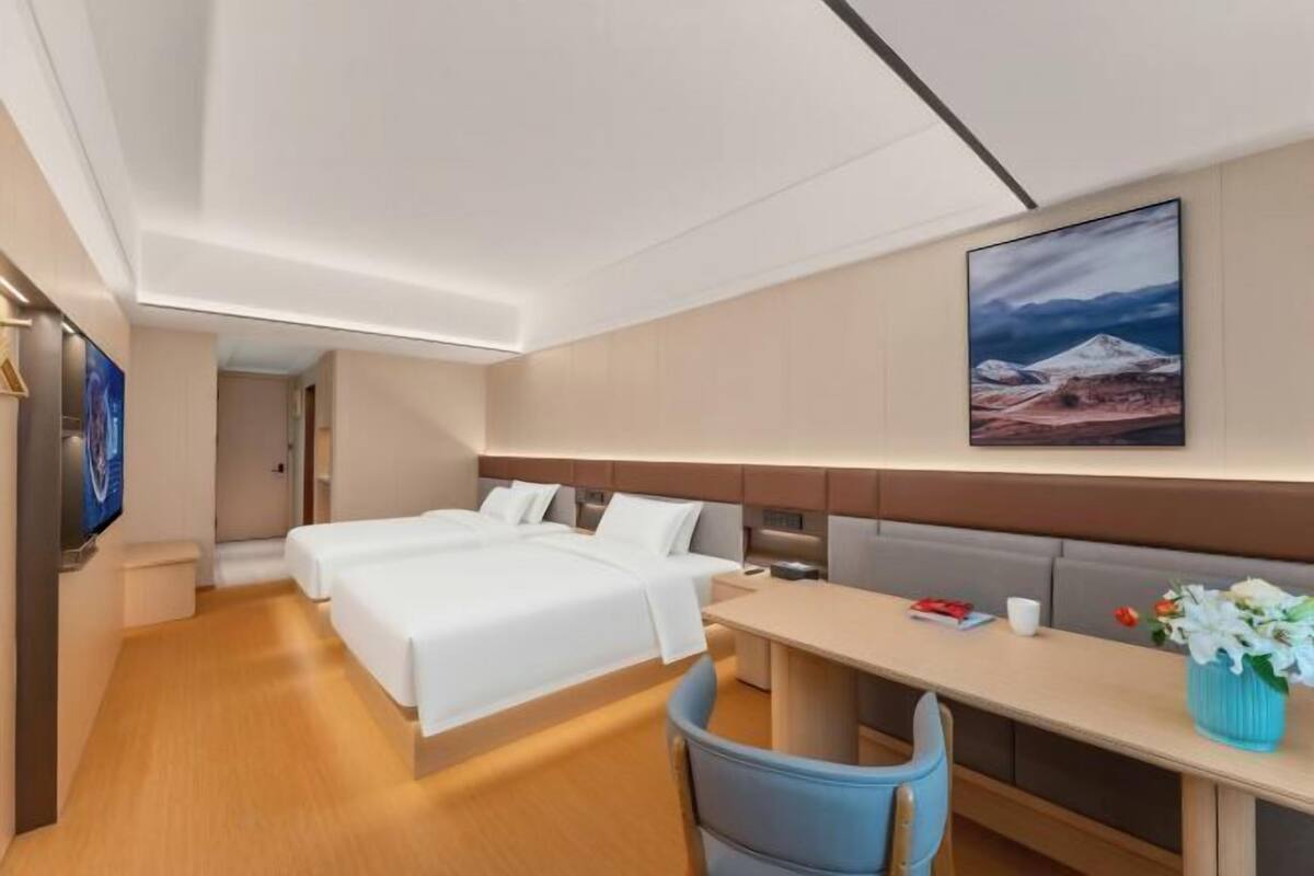 A hotel room with two beds, a desk, a chair, a TV, and a painting on the wall.
