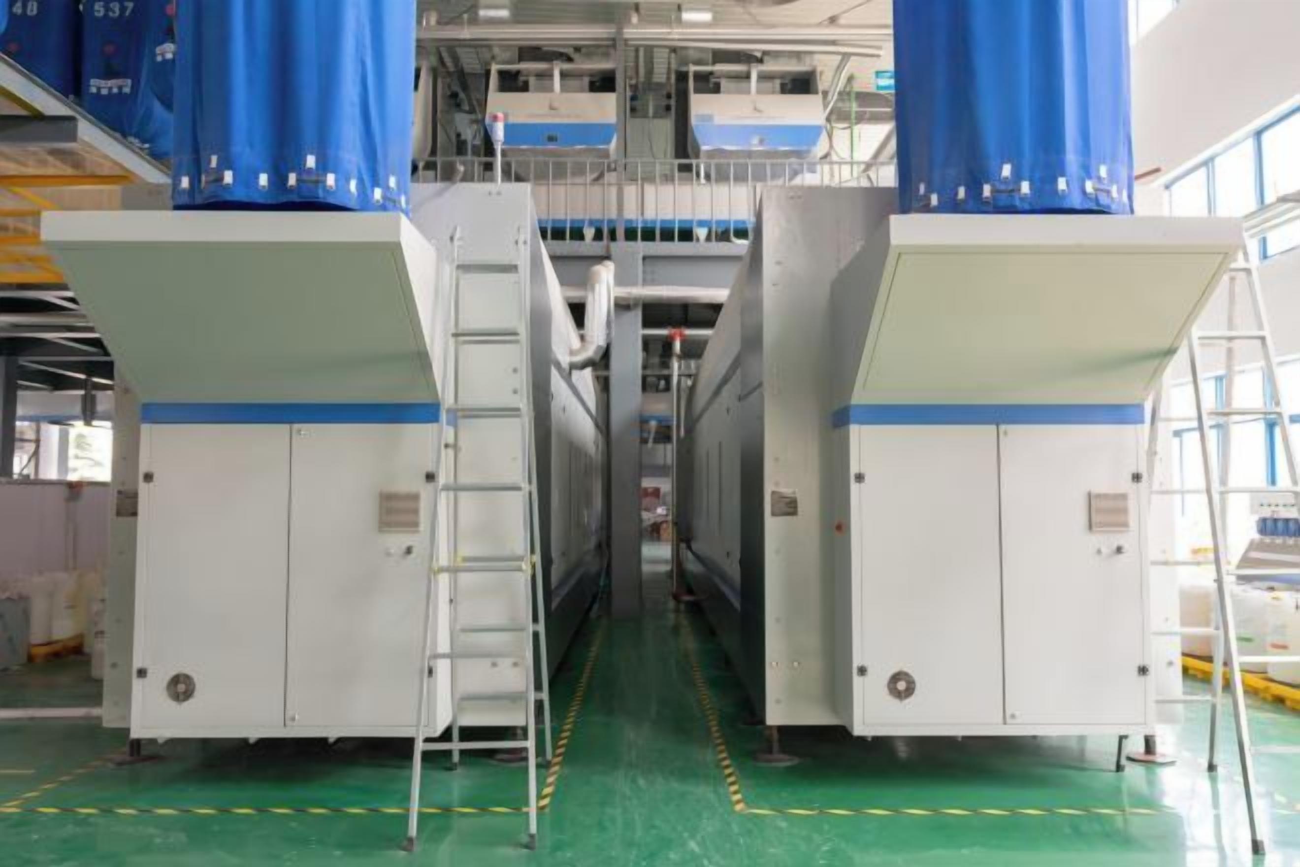 A large industrial facility with two large white machines, a central walkway, and blue curtains on top.