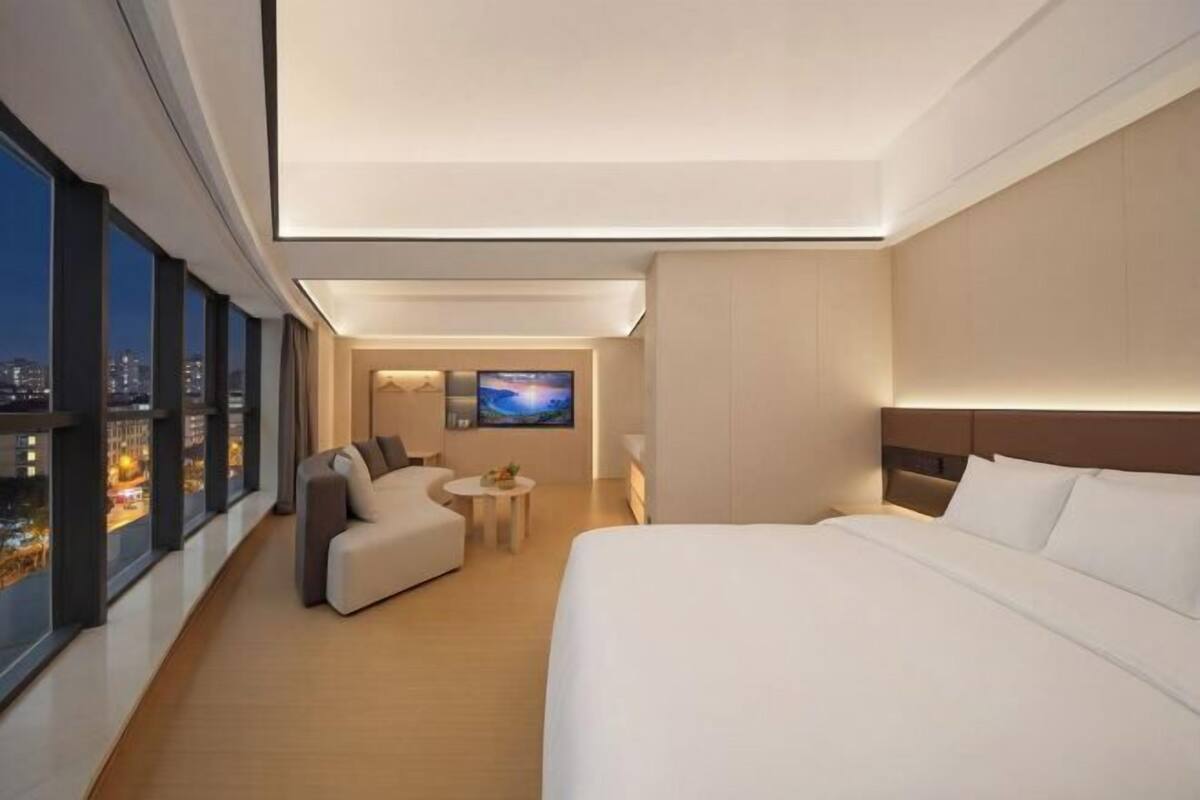 A modern hotel room with a large bed, a sofa, a small table, and a TV.