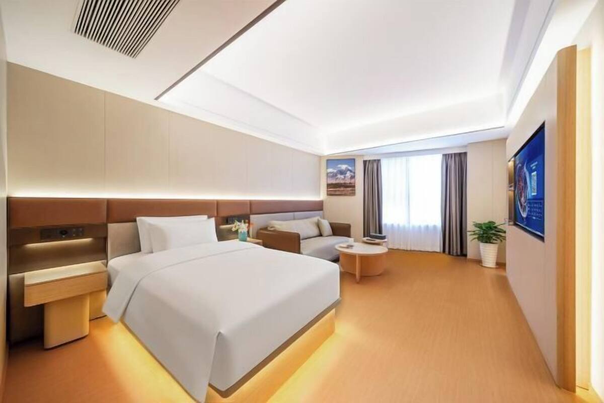 A modern hotel room with a large bed, bedside tables, a seating area, and a television.
