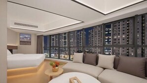 A modern hotel room with a large window, a sofa, a bed, and a small table with a vase of flowers. - Vienna Classic Hotel (Qingdao Golden Beach Wuyue Plaza) (Qingdao)