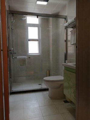 A bathroom with a glass-enclosed shower, a toilet, and a sink with a green cabinet. - Greentree Inn Tongchuan Yaozhou District New District Hospital Business Hotel (Tongchuan)