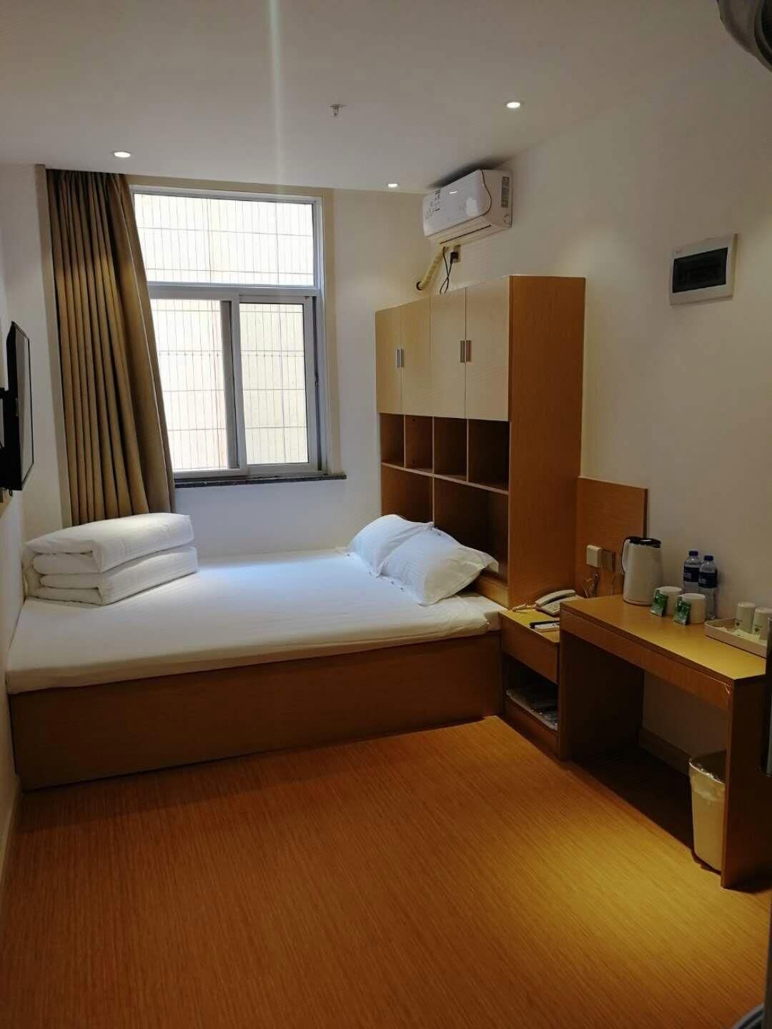 Una habitación de hotel con cama, escritorio, armario y ventana con cortinas.