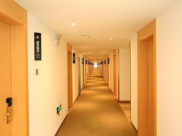 Un pasillo de hotel con puertas de madera, placas con números de habitación y suelo alfombrado.