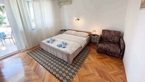 A bedroom with a bed, a chair, a small table, and a window with curtains.