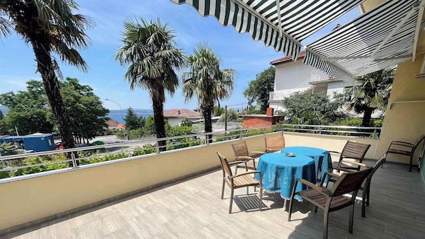 A balcony with a table and chairs, overlooking a residential area with palm trees and houses.
