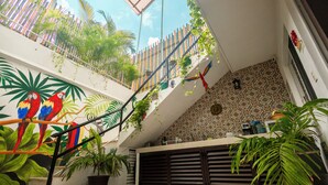 Ein mehrgeschossiges Interieur mit Treppe, Topfpflanzen und einem Wandgemälde bunter Papageien.