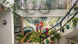 Eine Treppe mit Wandgemälde von Papageien und tropischer Vegetation, umgeben von Topfpflanzen und einem Bambuszaun.