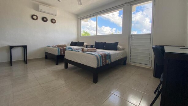 Ein Zimmer mit zwei Betten, einem Deckenventilator, einem Fenster mit Blick zum Himmel und einer Tür.