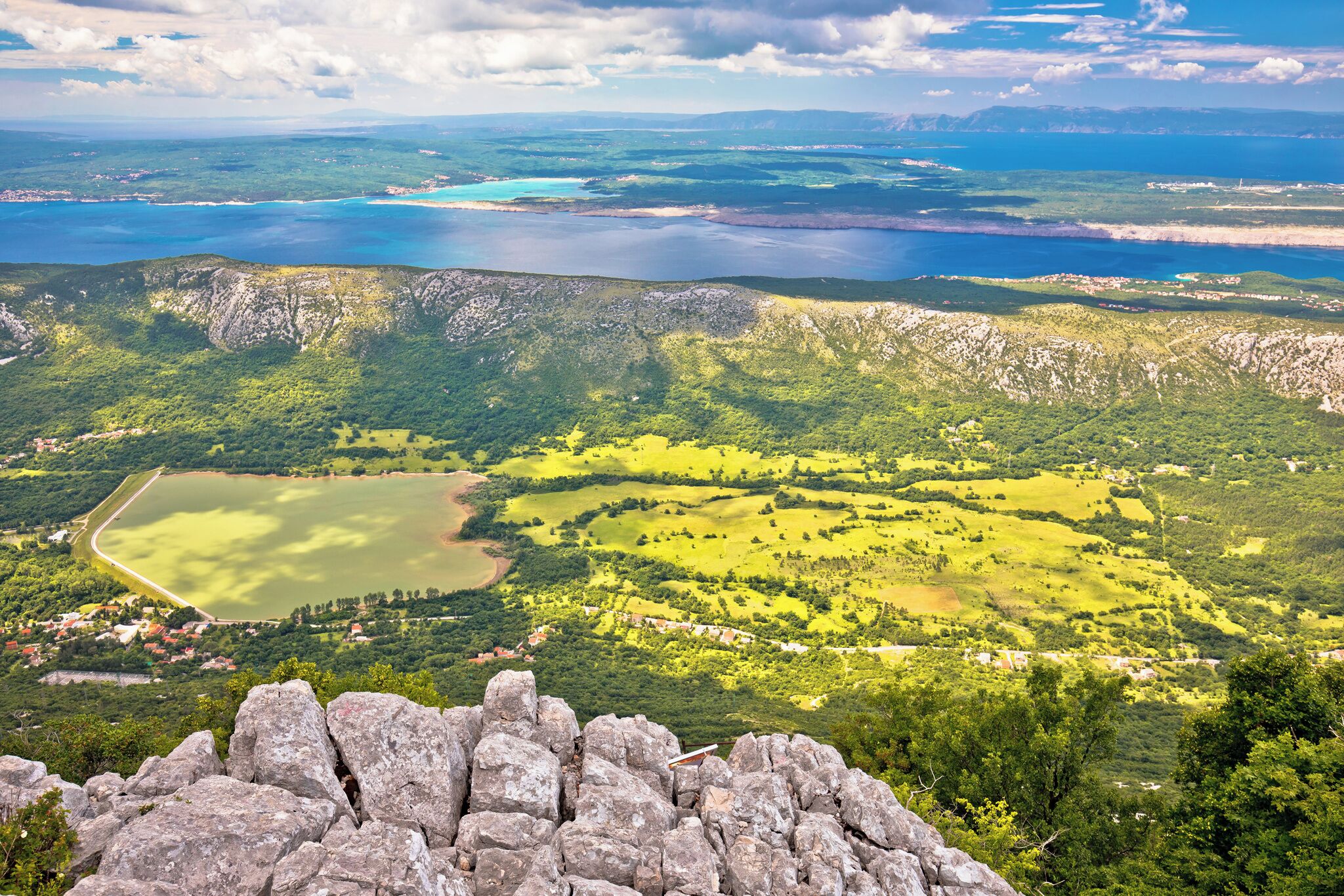 Vista panoramica su un paesaggio montuoso con un lago, zone boschive e un piccolo insediamento.