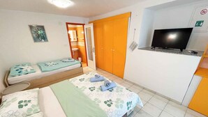 Quarto de hotel com duas camas, televisão e banheiro com porta laranja.
