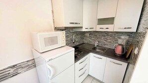 Cozinha compacta com armários brancos, micro-ondas, fogão a gás, pia e painel de fundo estampado.