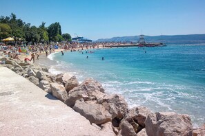 A beach with rocky shoreline, clear blue water, and people swimming and sunbathing. - Holiday apartment air-conditioned with Wi-Fi (Crikvenica)