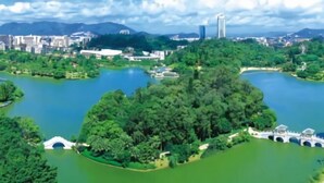 A park with a lake, bridges, and buildings in the background. - Jiangmen Park Lane Yiju Hotel (Wuyi University Jianshe Road) (Jiangmen)