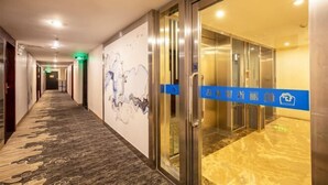A hotel corridor with a patterned carpet, a wall with abstract art, and an elevator area with a blue tape barrier. - Jiangmen Park Lane Yiju Hotel (Wuyi University Jianshe Road) (Jiangmen)