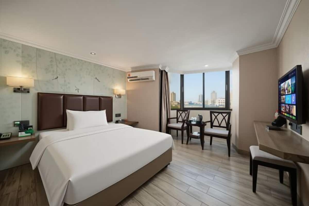 A hotel room with a large bed, a desk with a chair, a TV, and a city view.
