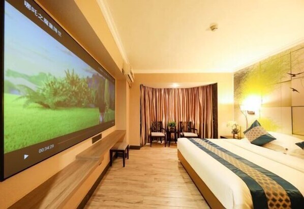 A hotel room with a large flat-screen TV mounted on the wall, a bed with a patterned bedspread, a bedside table with a lamp, and a window with curtains. - Jiangmen Park Lane Yiju Hotel (Wuyi University Jianshe Road) (Jiangmen)