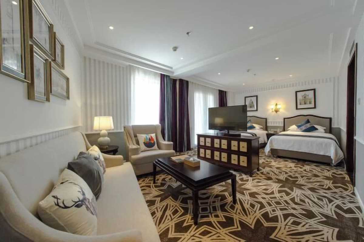 A hotel room with a sofa, armchair, TV, and two beds.