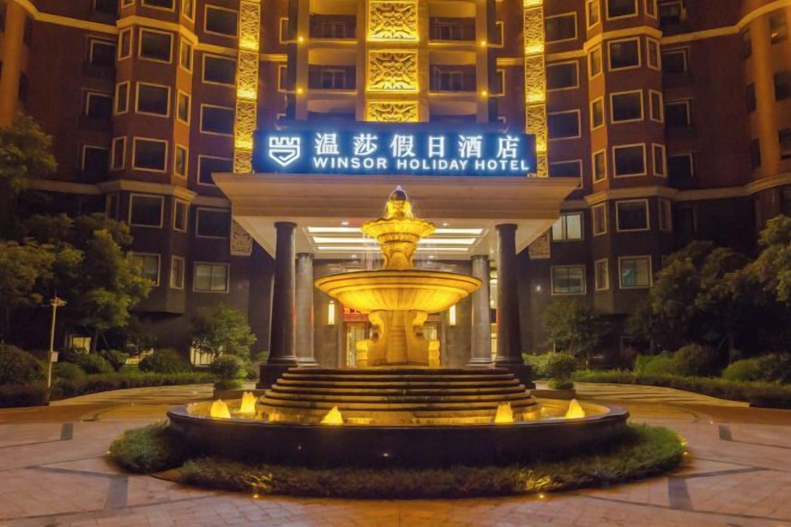 A hotel entrance with a fountain, a signboard, and a well-maintained garden.