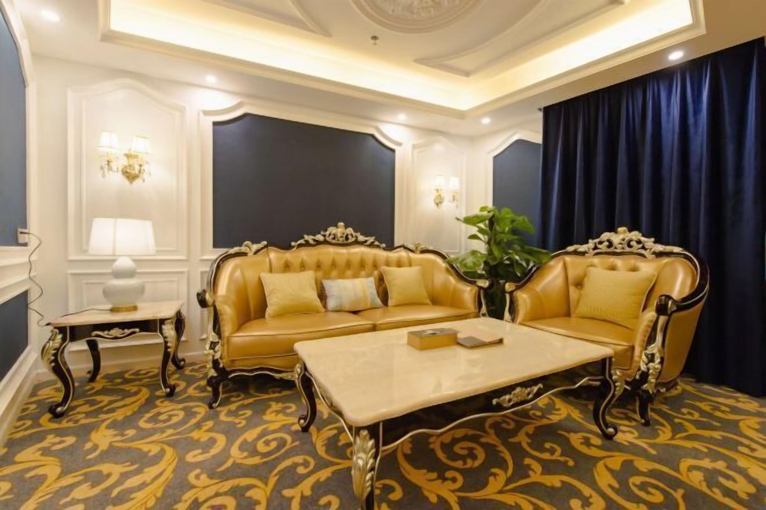 Quarto luxuoso com sofá bege, uma poltrona combinando e uma mesa de centro. Há um tapete estampado e uma janela grande com cortinas.