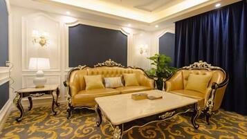 Quarto luxuoso com sofá bege, uma poltrona combinando e uma mesa de centro. Há um tapete estampado e uma janela grande com cortinas.