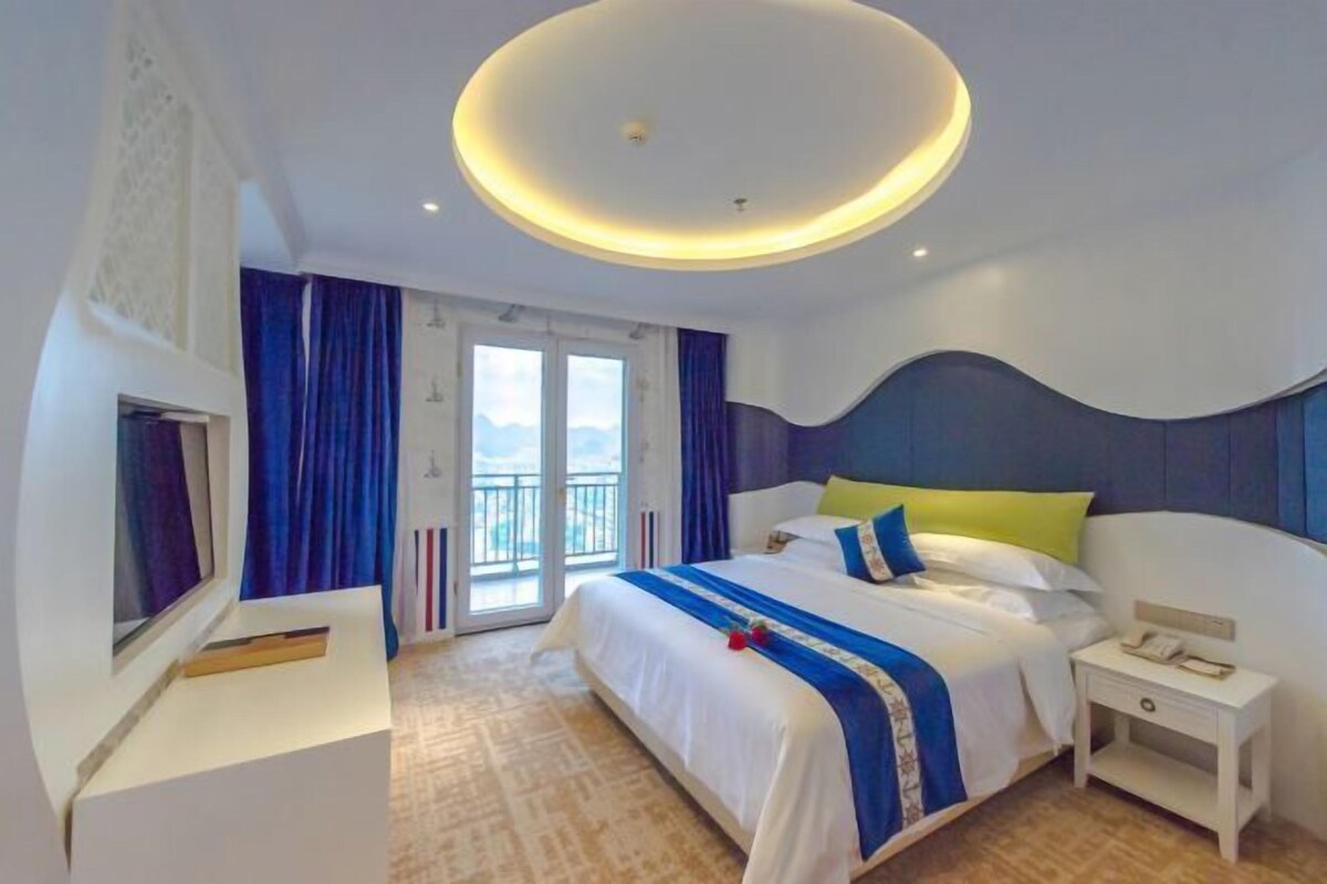 A modern hotel room with a large bed, a bedside table, a desk, and a view of the outdoors.