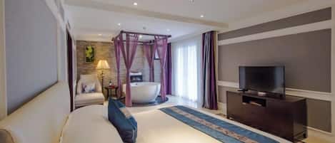A hotel room with a large bed, a flat-screen TV, a bathtub, and a seating area with a lamp.