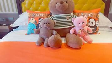 A bed with a yellow tufted headboard, two pillows with a zoo theme, and three plush toys on the bed.