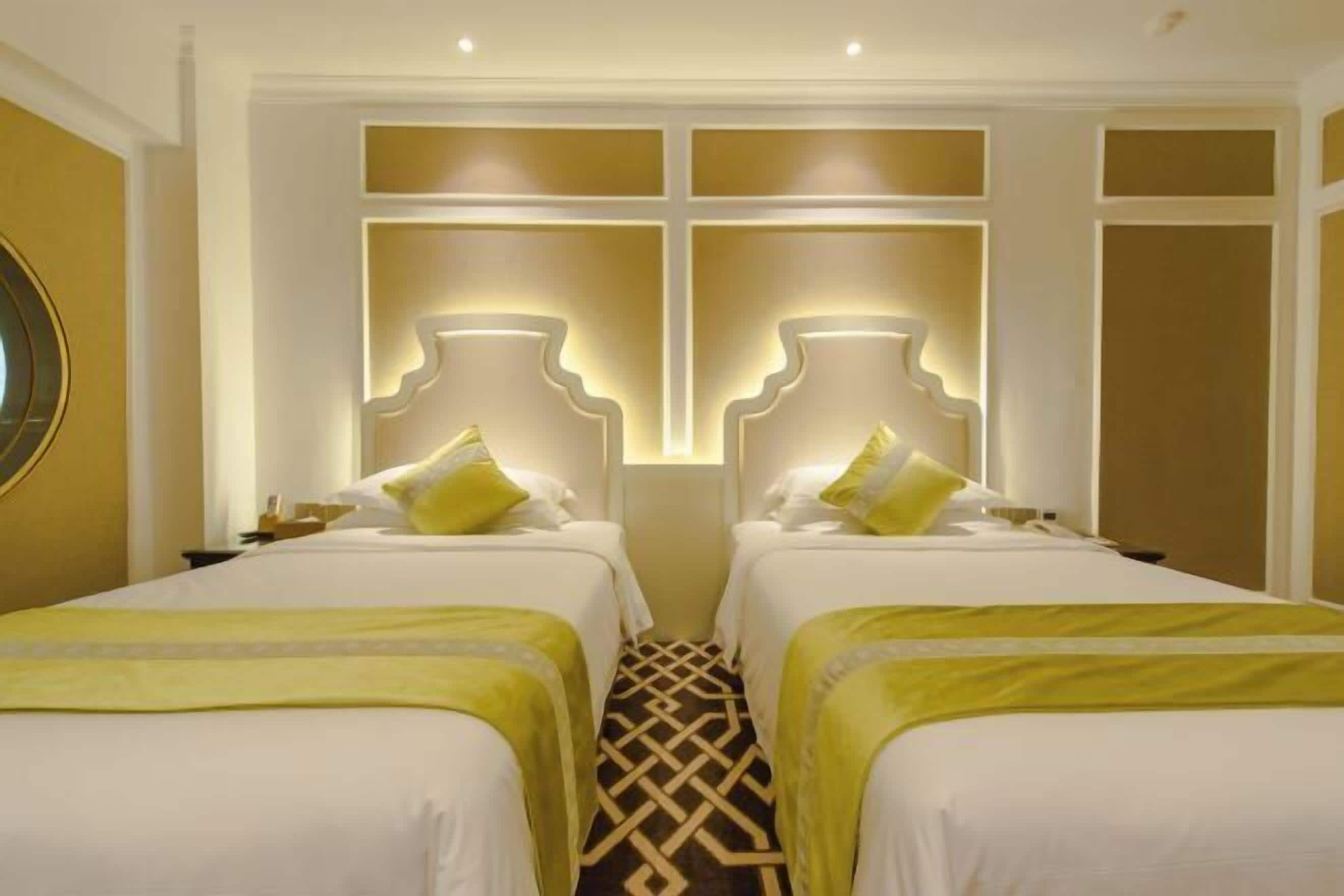 Ett hotellrum med två sängar, ett mönstrat golv och en dekorativ väggpanel.