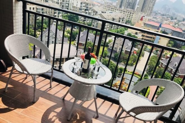 A balcony with wicker chairs and a small table, overlooking a cityscape.