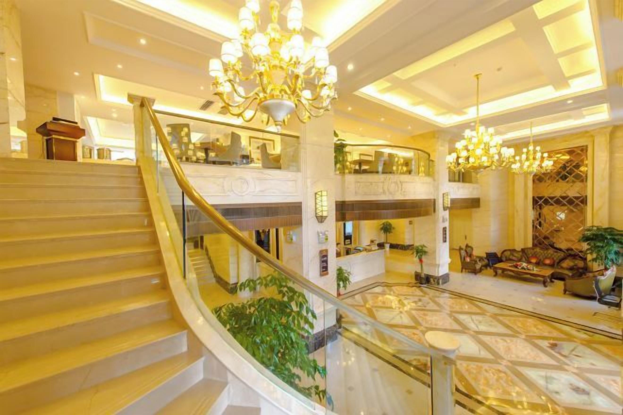 Un ampli vestíbul d'hotel amb un espaiós atrium, una imponent escala i elegants llumaires.