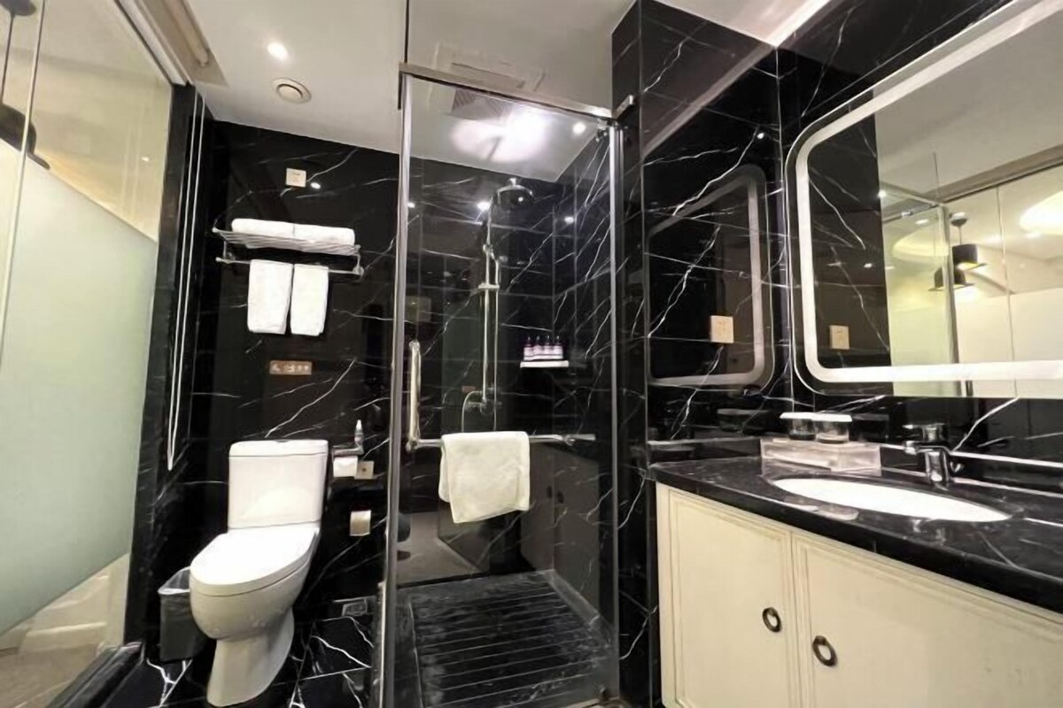 A modern bathroom with a black marble wall, a white toilet, a glass-enclosed shower, and a large mirror.