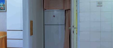 A compact kitchen with a white refrigerator, a wooden cabinet, and a tiled backsplash.