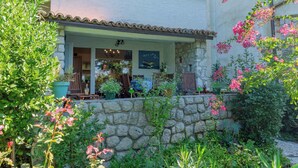 A stone wall with a garden in front of a building with a tiled roof and a window displaying various items. - Holiday apartment with large terrace (Jadranovo)